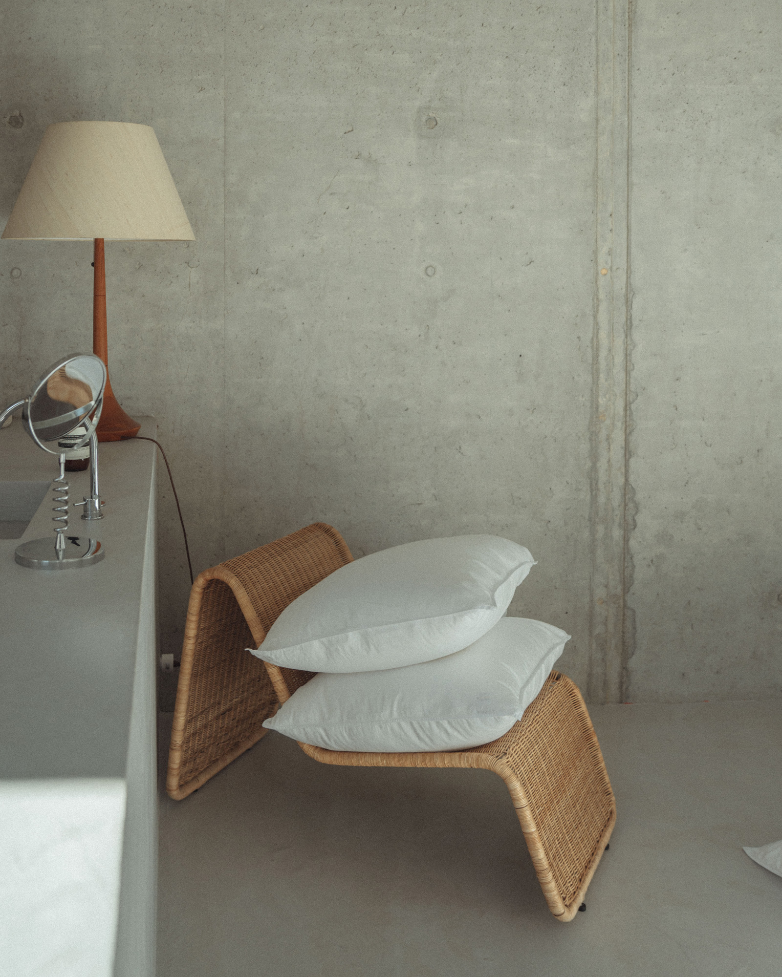 Minimalistische ruimte met rotan relaxstoel met stapel kussens in witte satijn